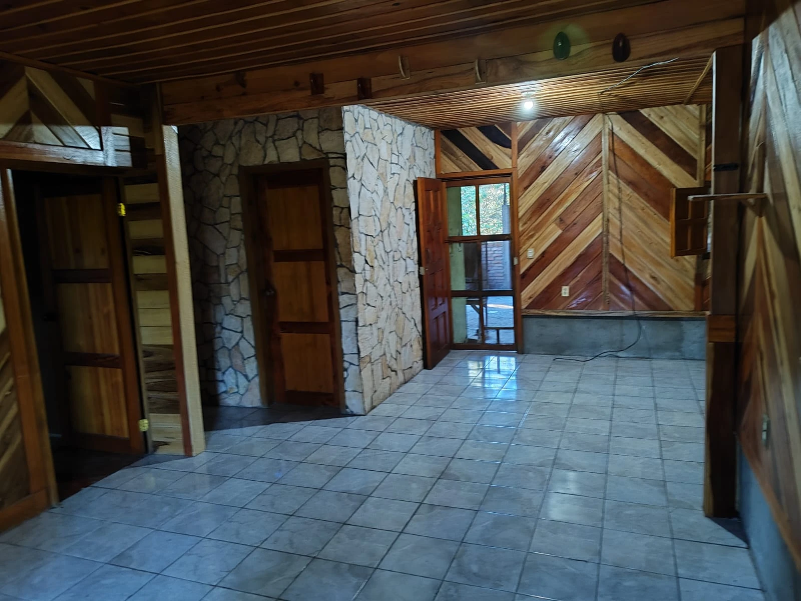 nterior de cabaña de madera con piso cerámico, paredes rústicas y acceso a habitaciones