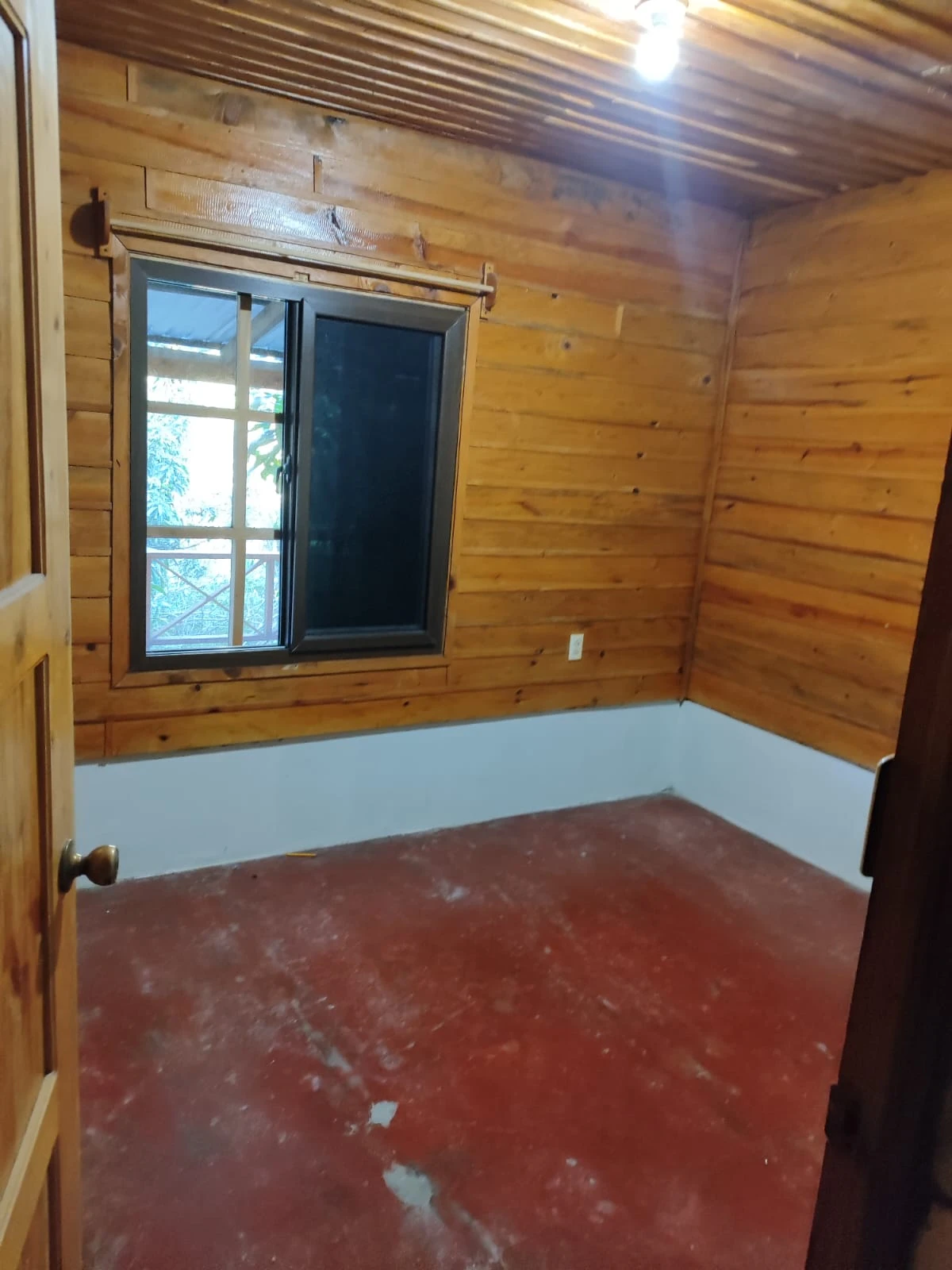 Habitación de cabaña de madera con ventana, iluminación natural y acabados rústicos