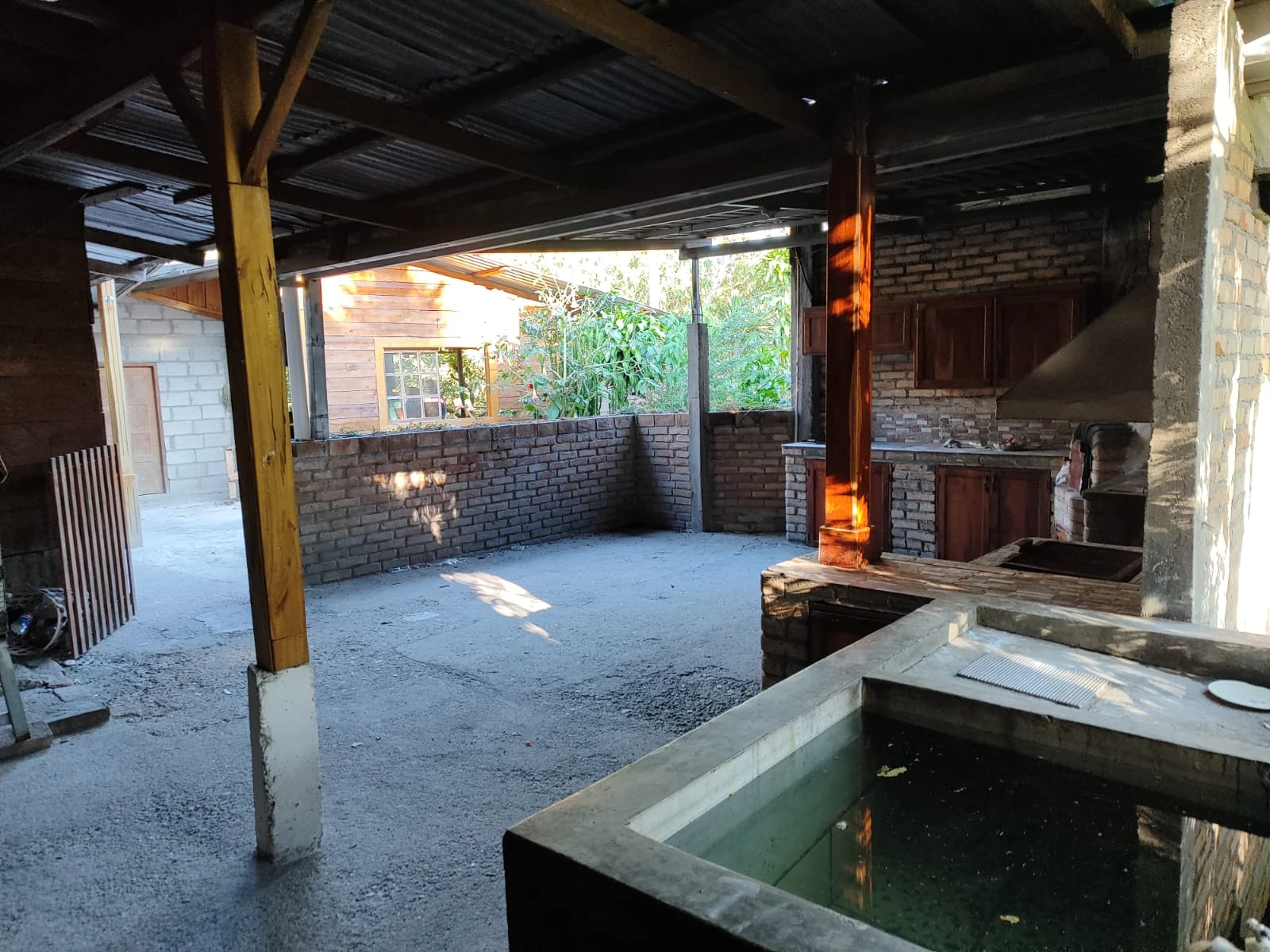 Área social techada con cocina rústica, parrilla y fregadero en propiedad rodeada de naturaleza