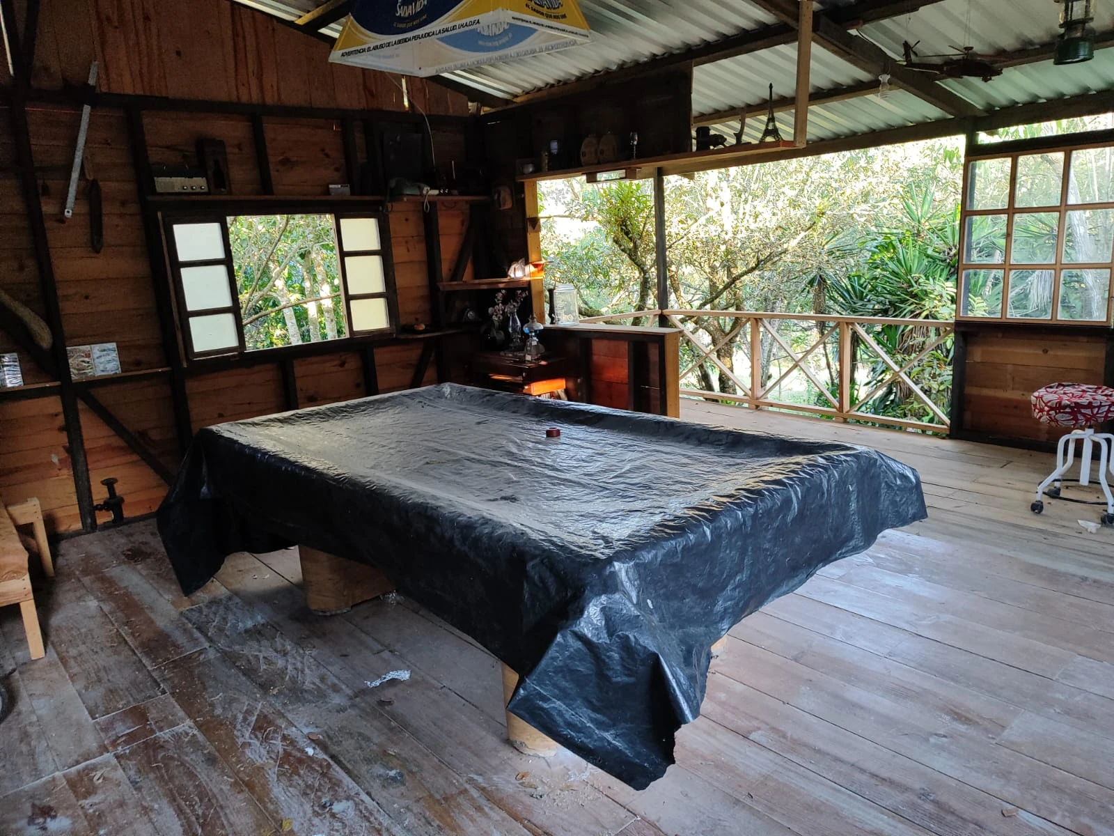 Sala rústica de cabaña de madera con mesa central y vista al bosque a través de ventanales