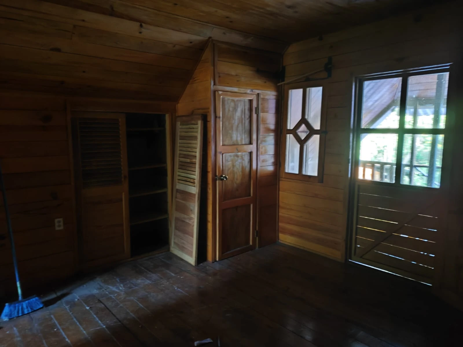 Habitación interior de cabaña de madera con puertas rústicas, ventana y acceso a balcón