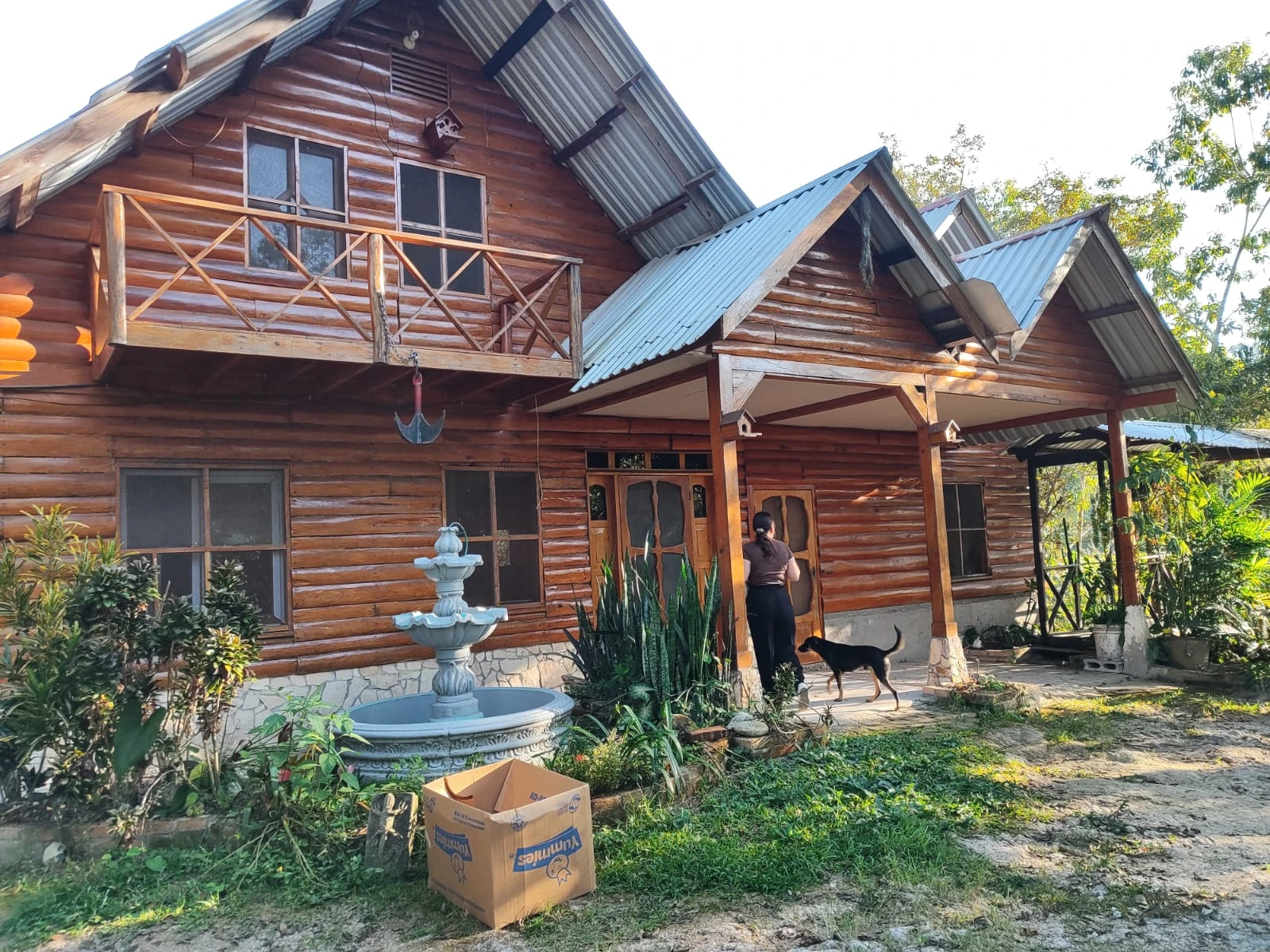 Cabaña de madera rústica con balcón y jardín frontal rodeado de vegetación natural
